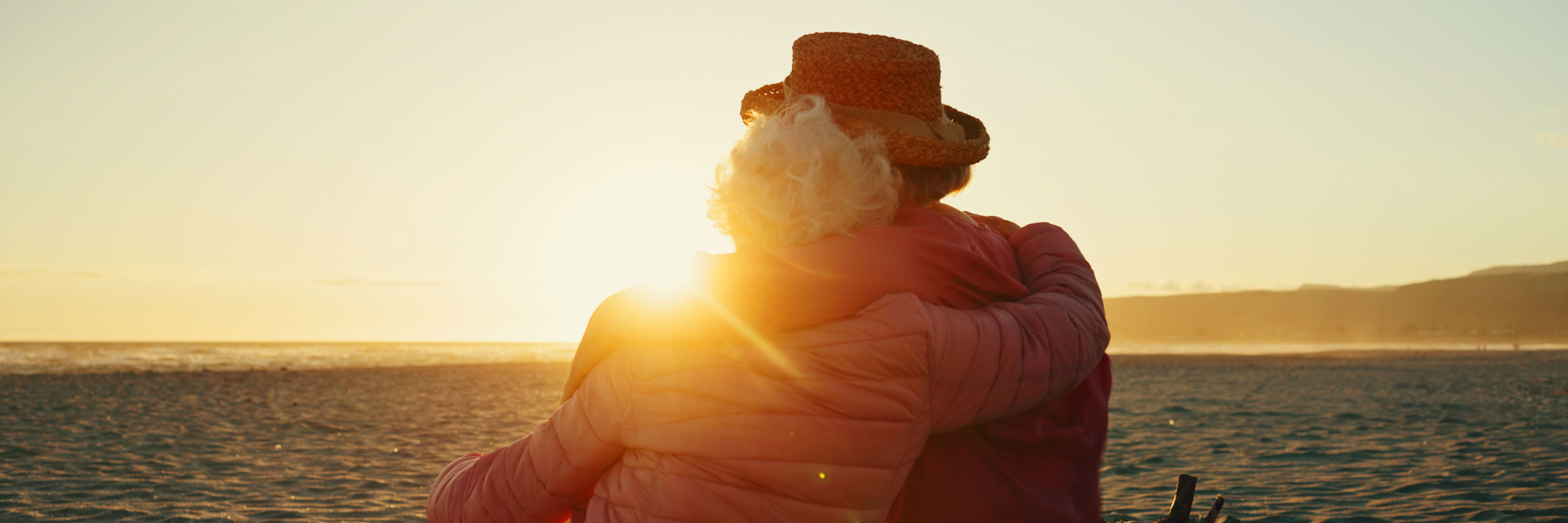 Ældre par holder om hinanden og kigger ud over havet i solnedgang