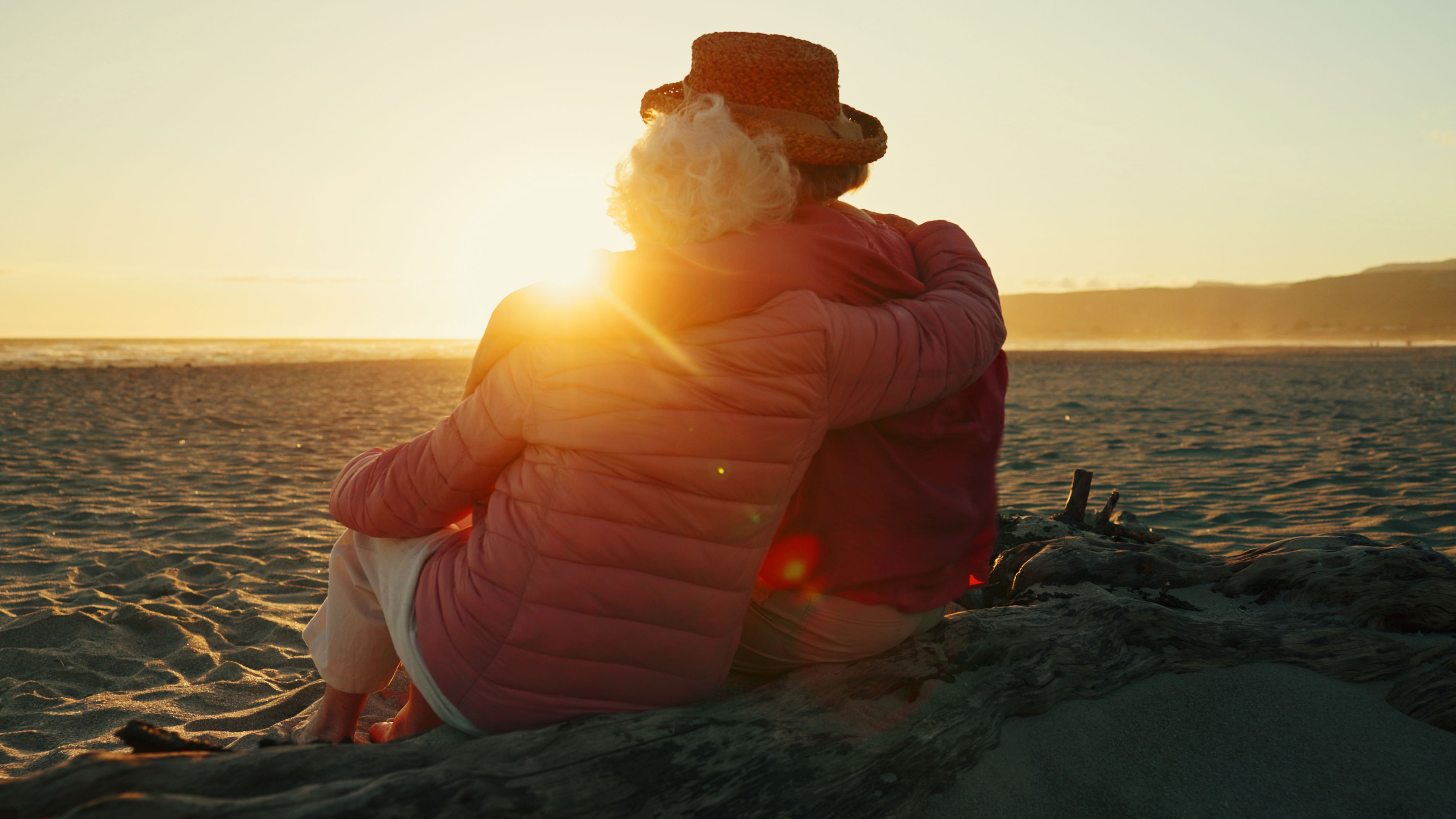 Ældre par holder om hinanden og kigger ud over havet i solnedgang