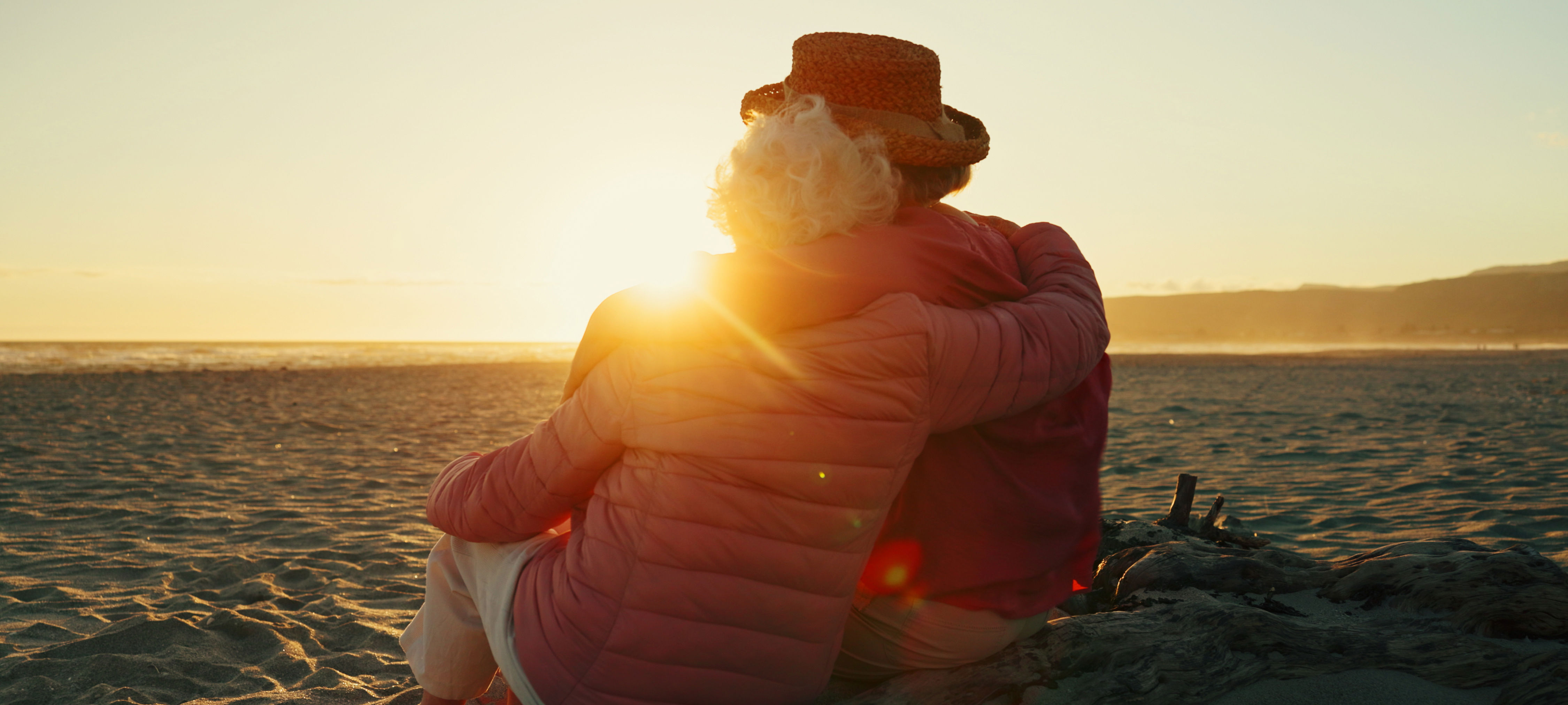 Ældre par holder om hinanden og kigger ud over havet i solnedgang
