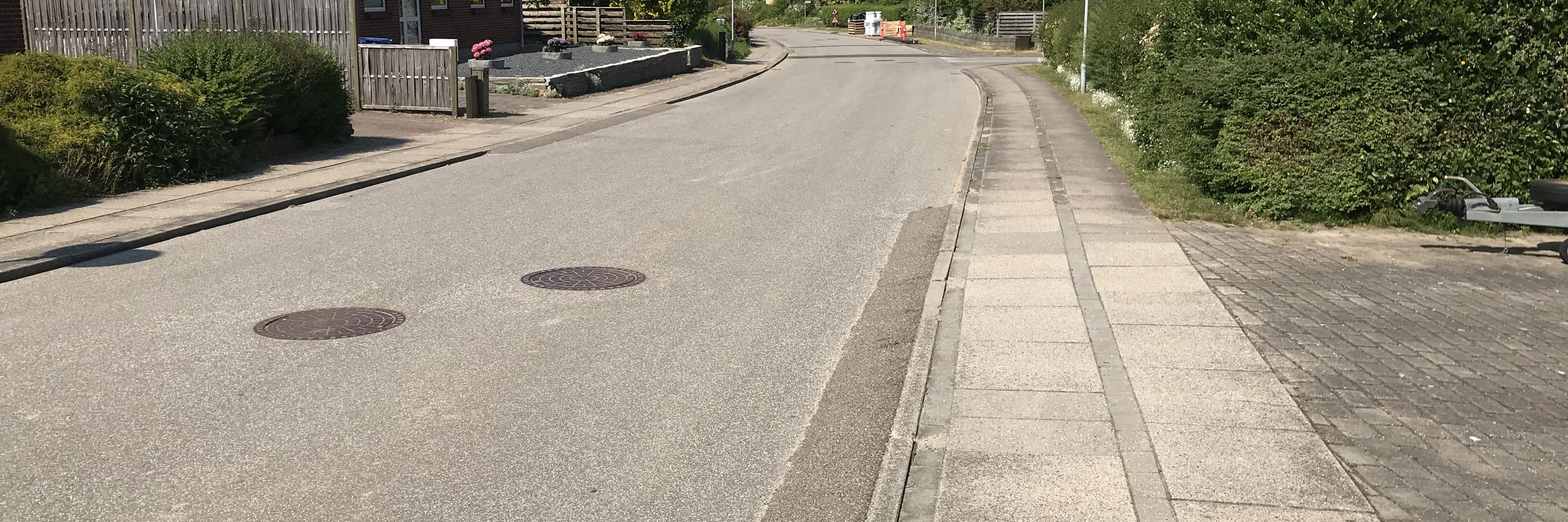 Villavej med kørebane og fortov med klassiske fortovsfliser - hækkene er grønne og himlen blå