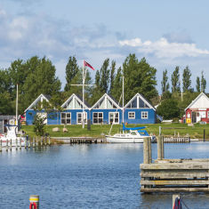 Indsejling til lystbådehavnen. Både der ligger til kaj. Bagerst rødt hus der huser havnekontoret og et blåt hus der huser sejlklubben.