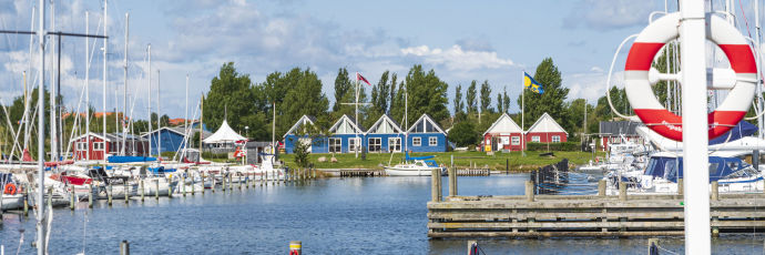 Indsejling til lystbådehavnen. Både der ligger til kaj. Bagerst rødt hus der huser havnekontoret og et blåt hus der huser sejlklubben.
