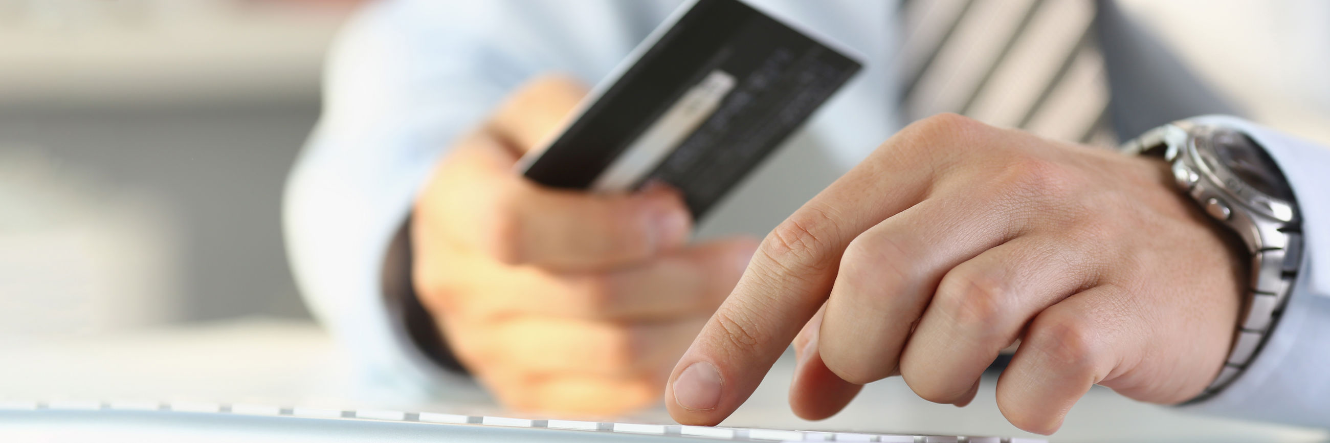 To hænder - den ene holder et kreditkort og den anden hviler på et tastatur