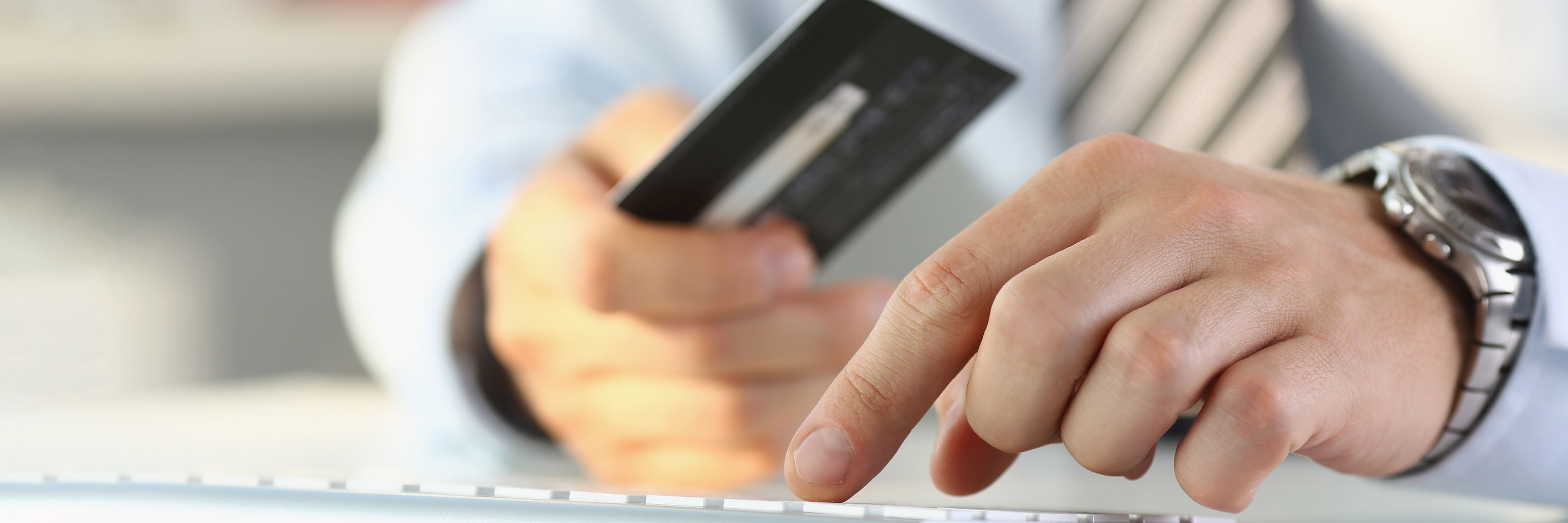 To hænder - den ene holder et kreditkort og den anden hviler på et tastatur