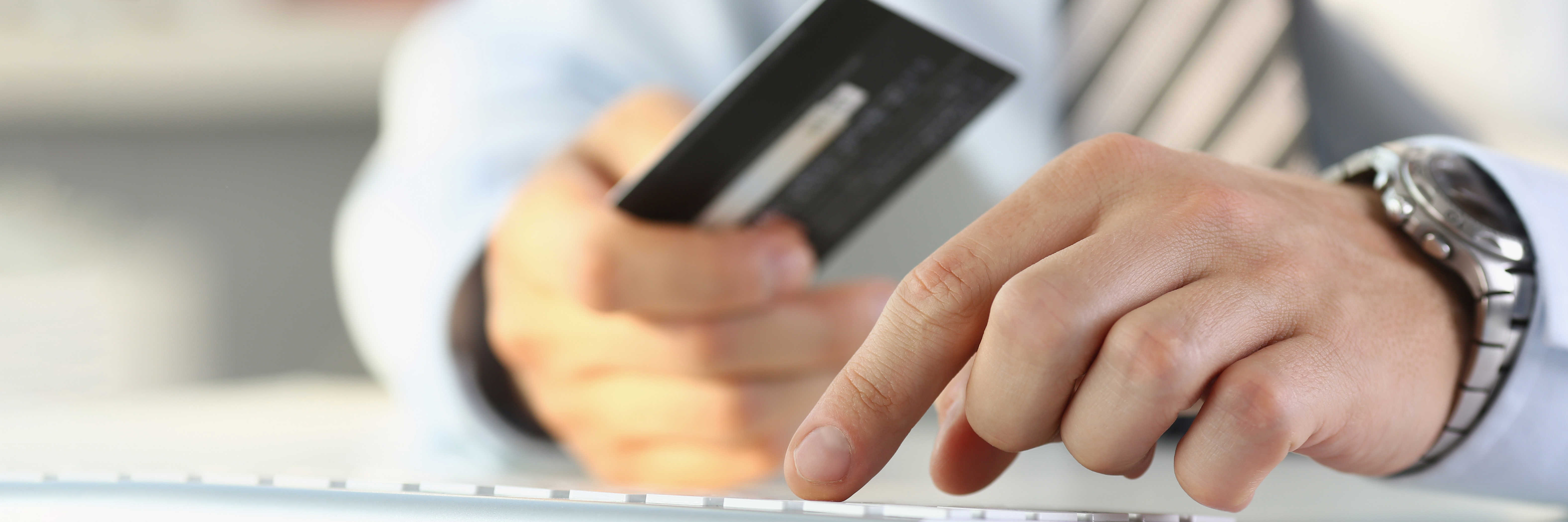 To hænder - den ene holder et kreditkort og den anden hviler på et tastatur