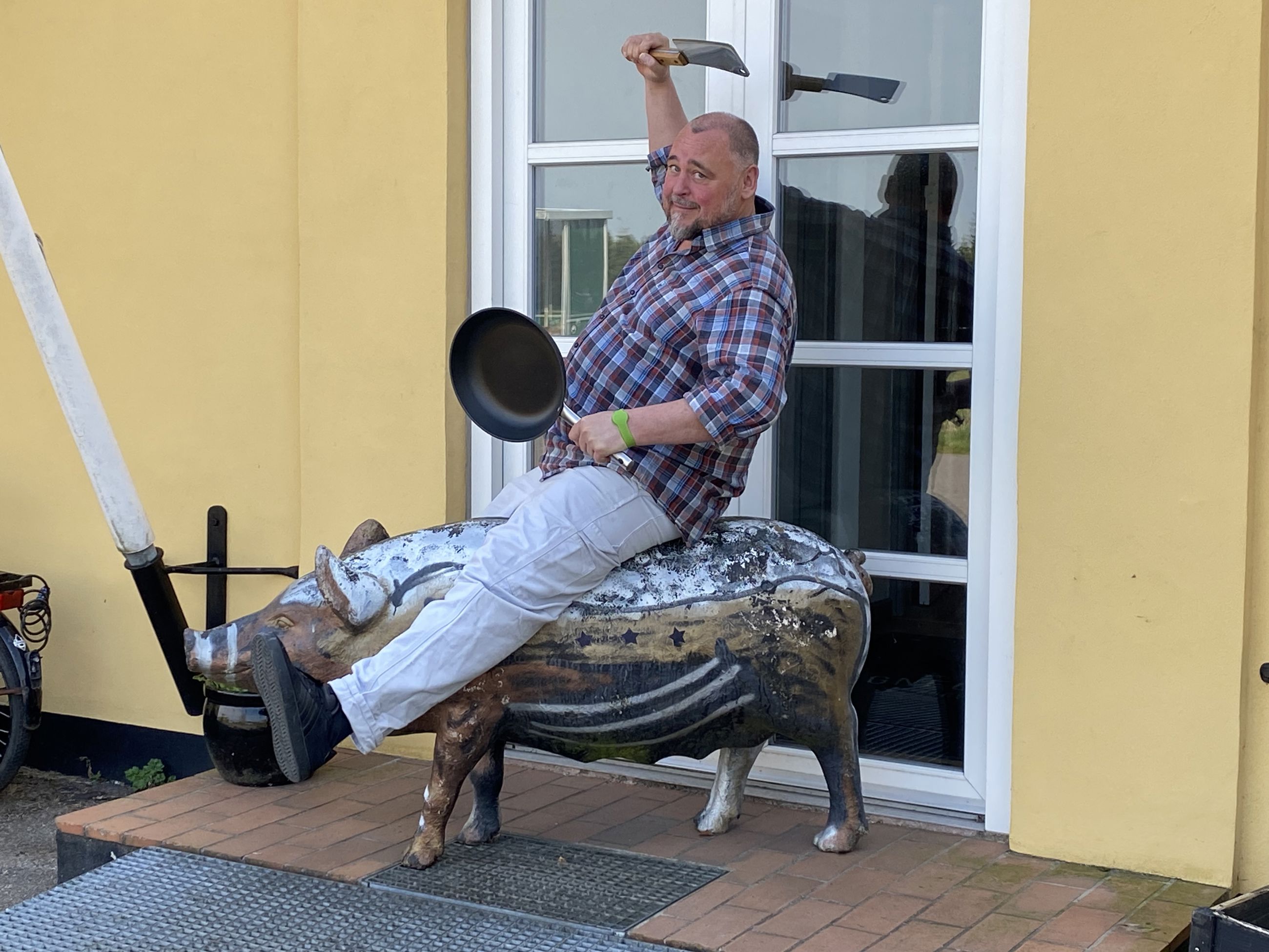 Mand der rider på en plastikgris med en stegepande og en kødkniv i hænderne