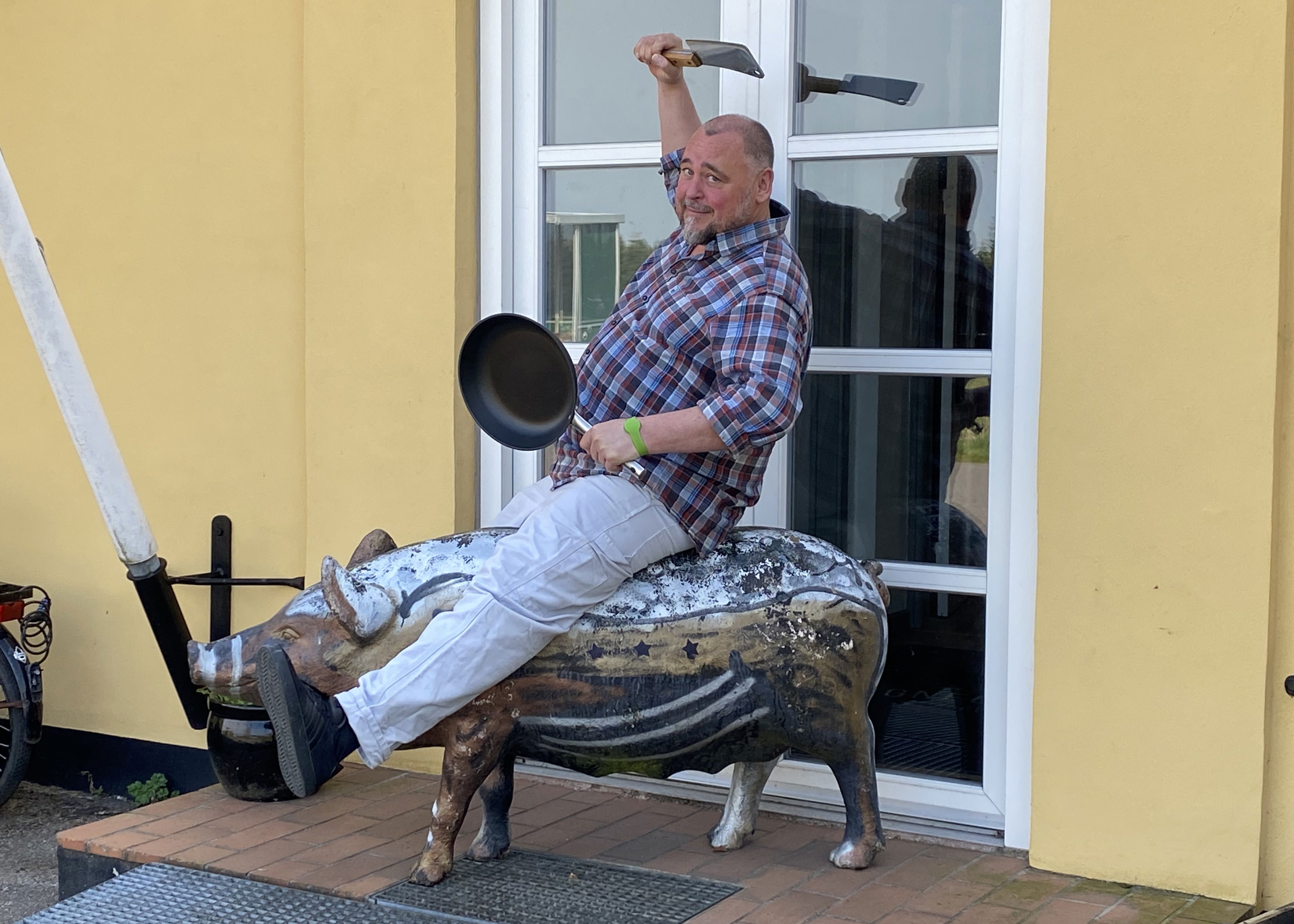 Mand der rider på en plastikgris med en stegepande og en kødkniv i hænderne