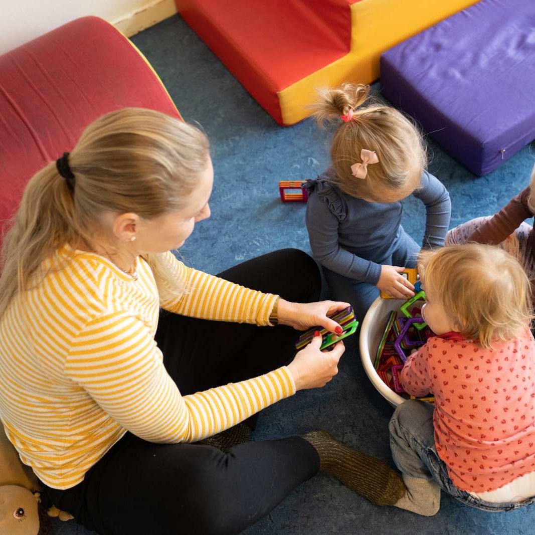 En studerende sidder og leger med tre små børn