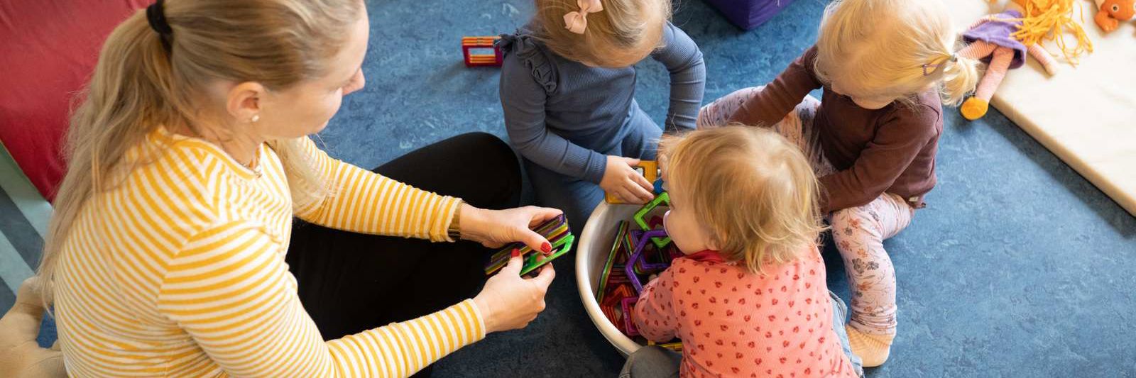 En studerende sidder og leger med tre små børn