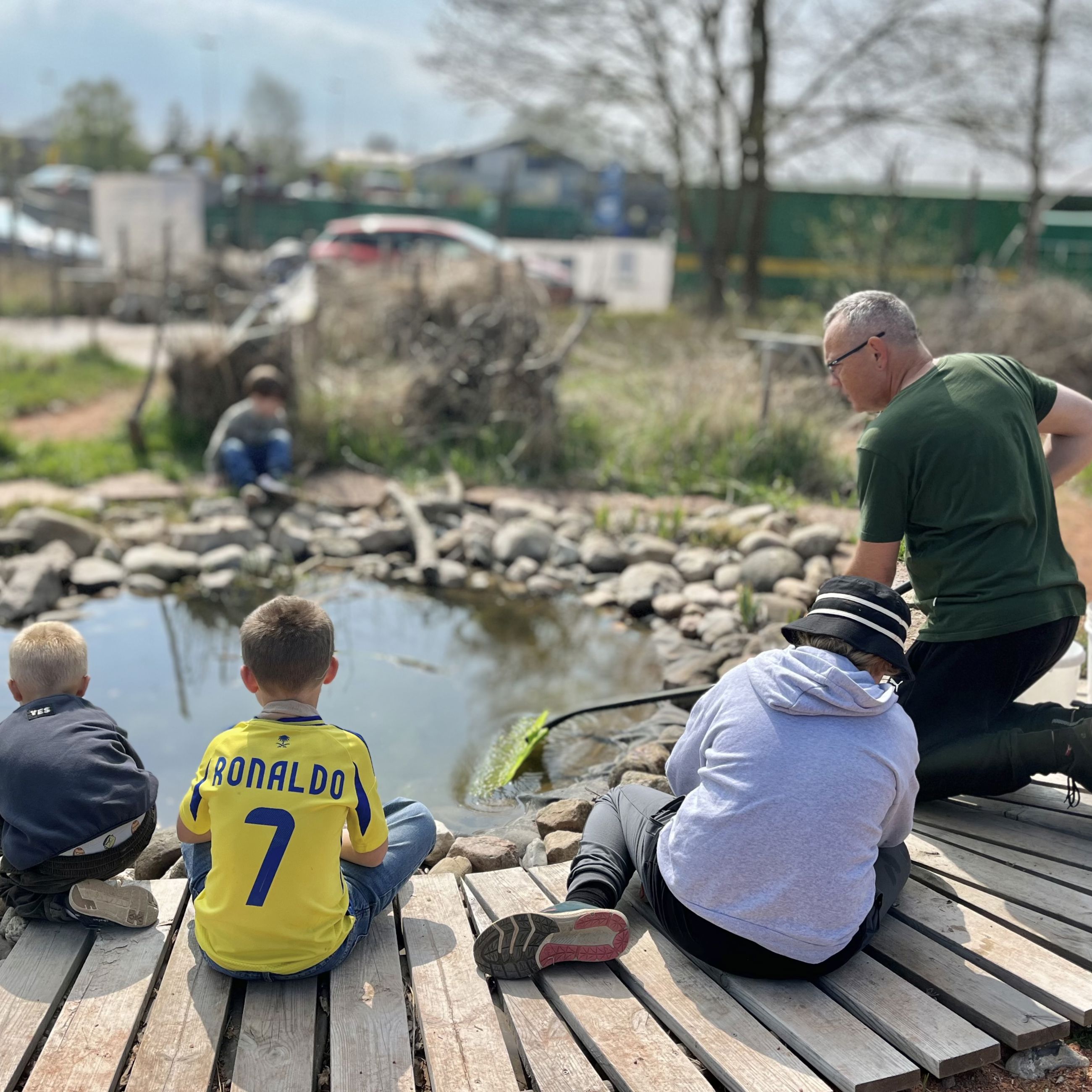 En voksen og flere børn der sidder ved fiskesøen på GenGRO