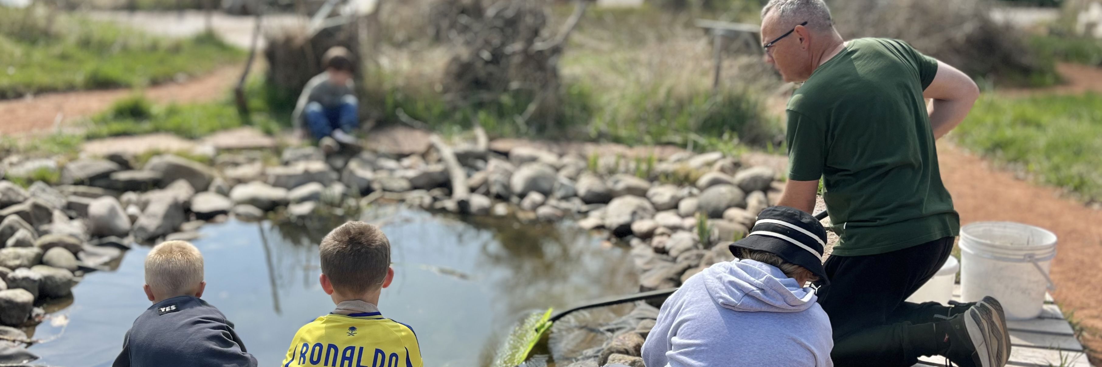 En voksen og flere børn der sidder ved fiskesøen på GenGRO