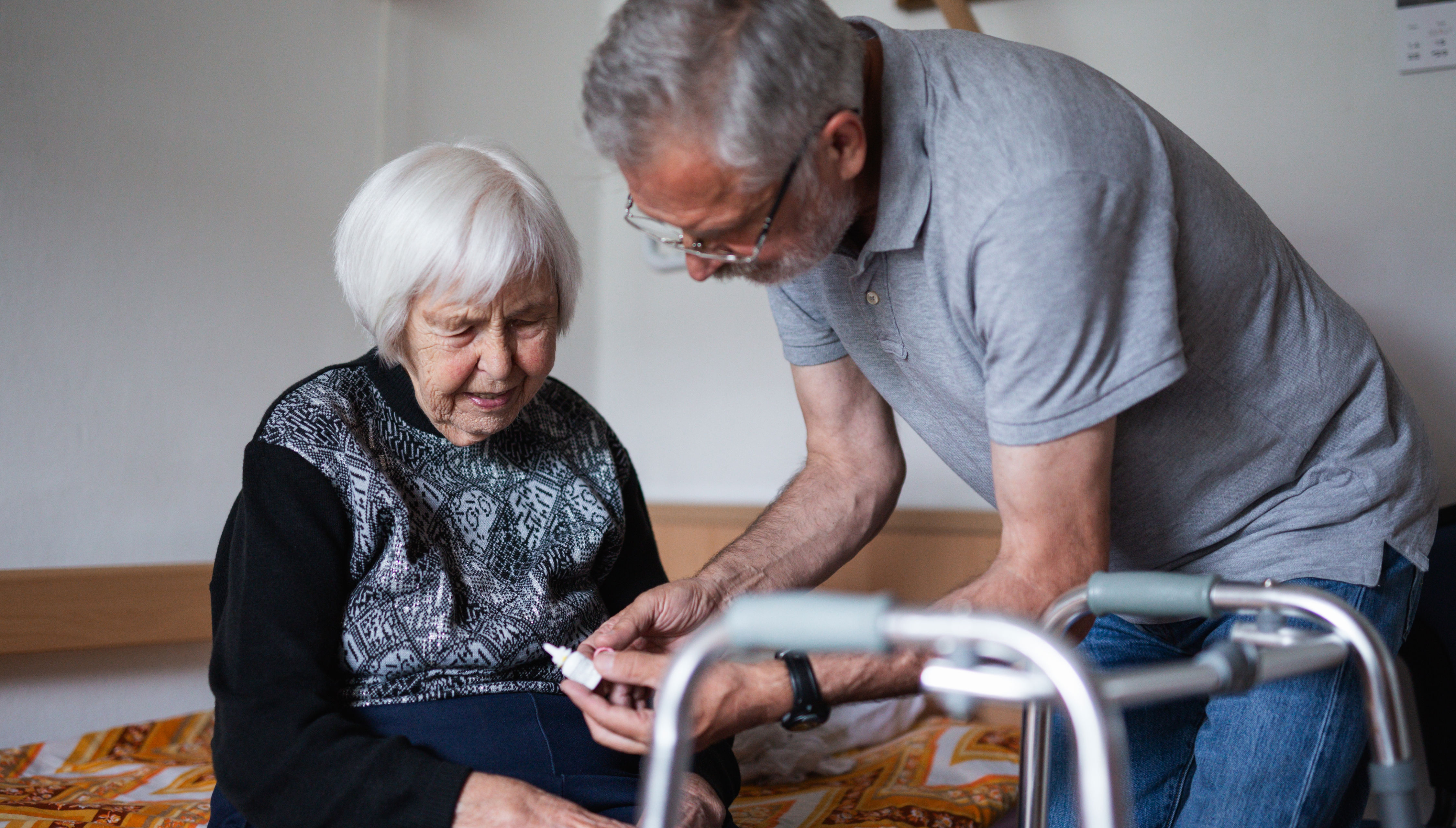 Frivillig mand taler med ældre kvinde, som sidder på en seng med sin rollator foran sig
