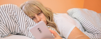 Kvinder der ligger i sengen og kigger på telefonen, fordi hun ikke kan sove grundet stress