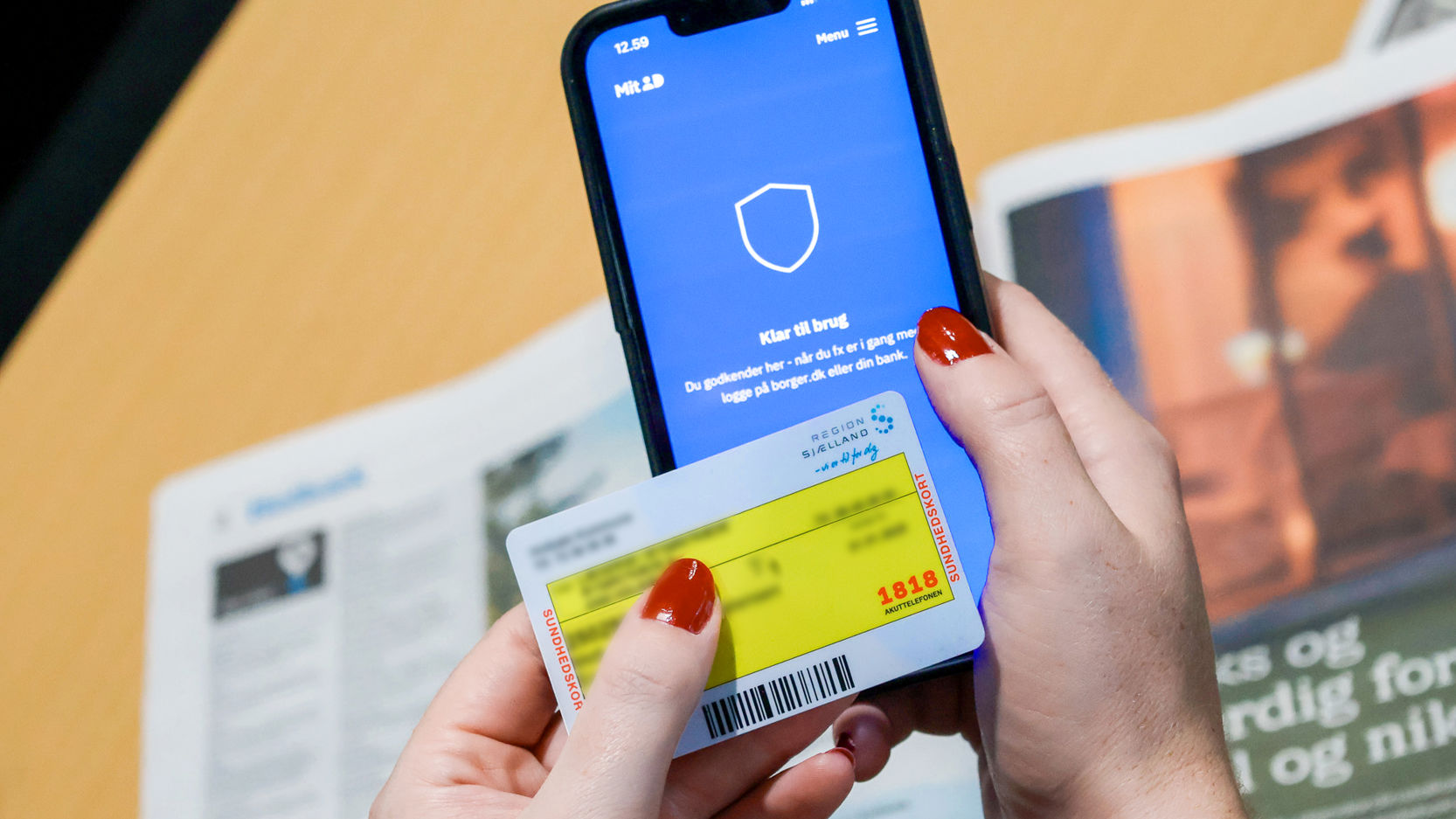 Kvindehænder holder sundhedskort foran telefon med mitid