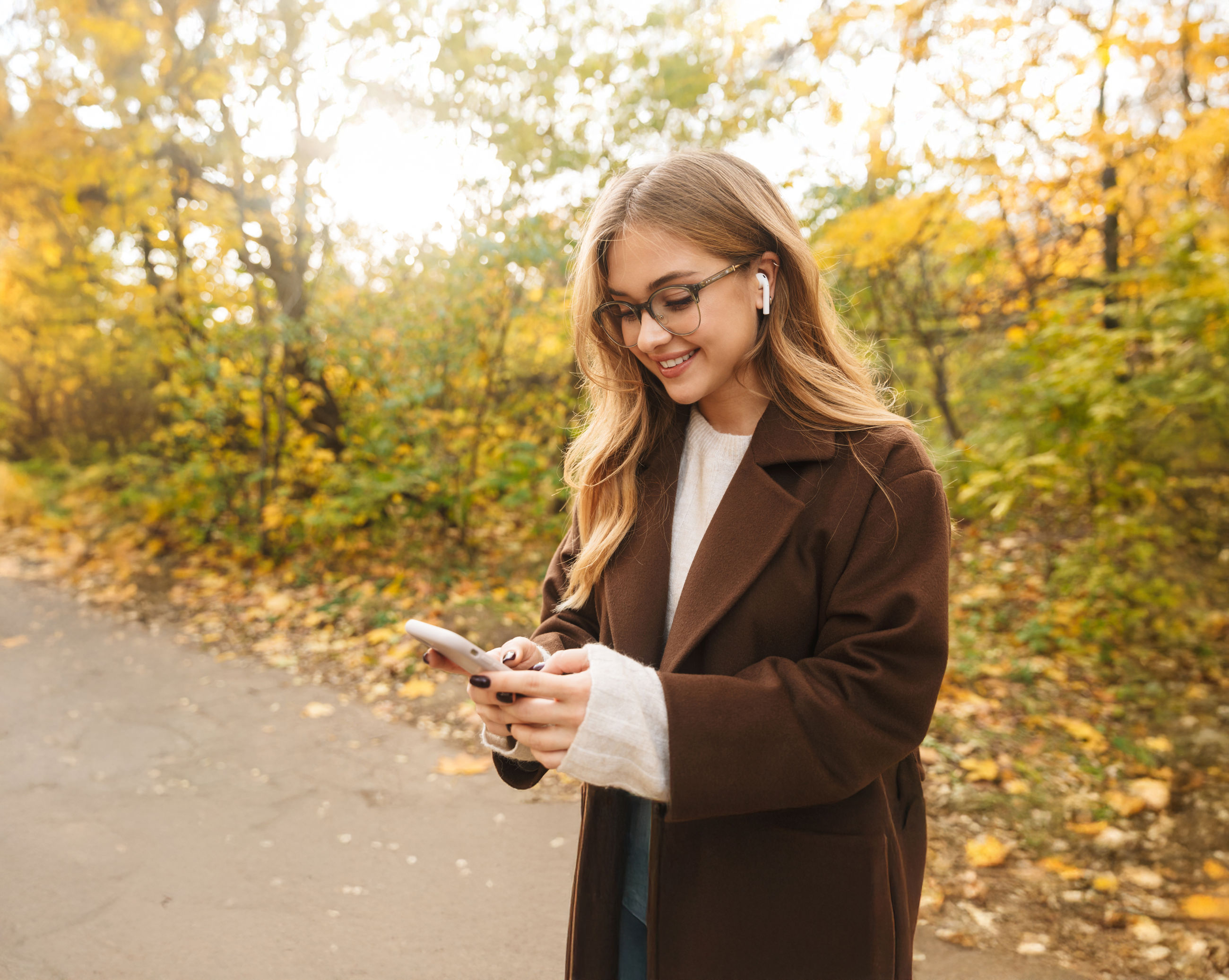 Ung kvinde der står på en skovsti med mobiltelefon og airpods