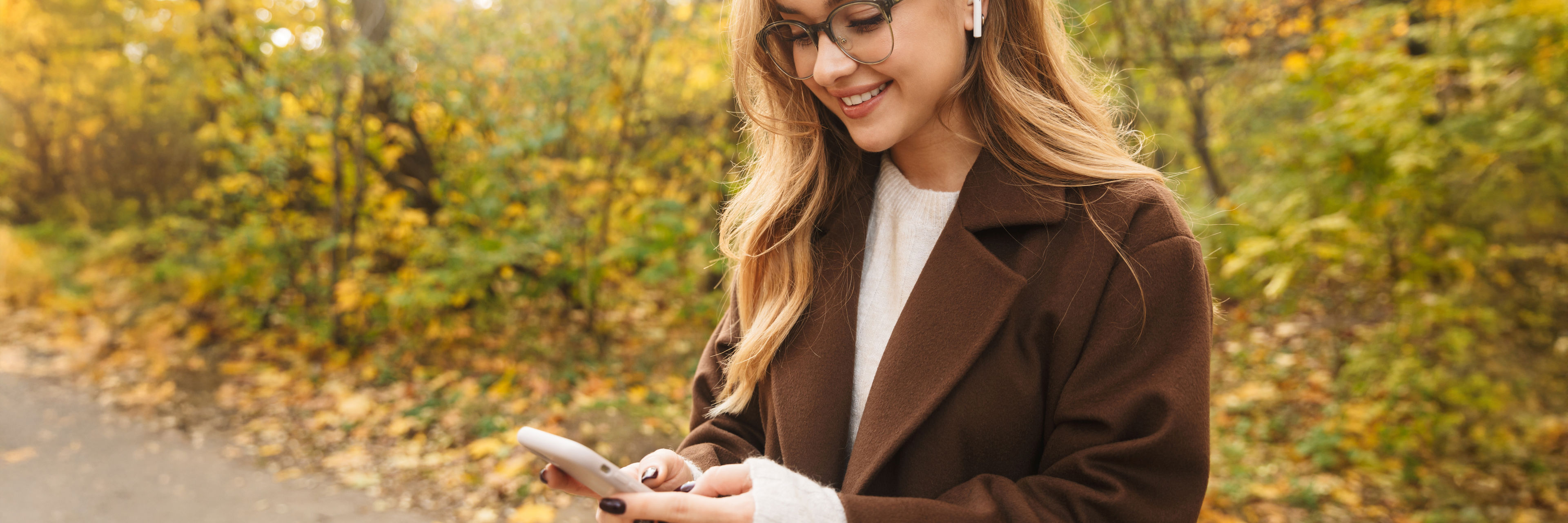 Ung kvinde der står på en skovsti med mobiltelefon og airpods