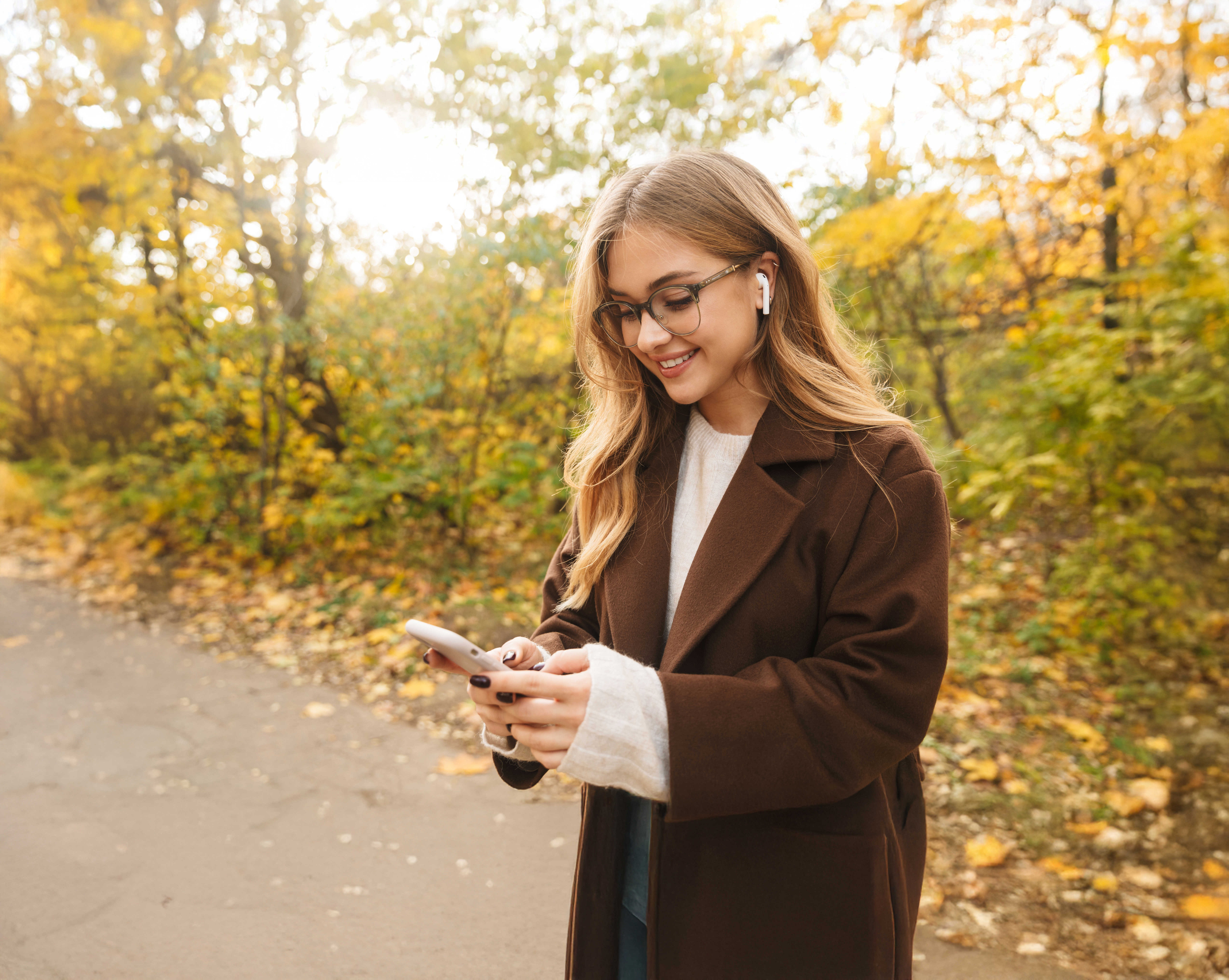 Ung kvinde der står på en skovsti med mobiltelefon og airpods
