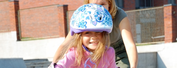 En voksen, der hjælper et barn, der står på rulleskøjter. Alle smiler.