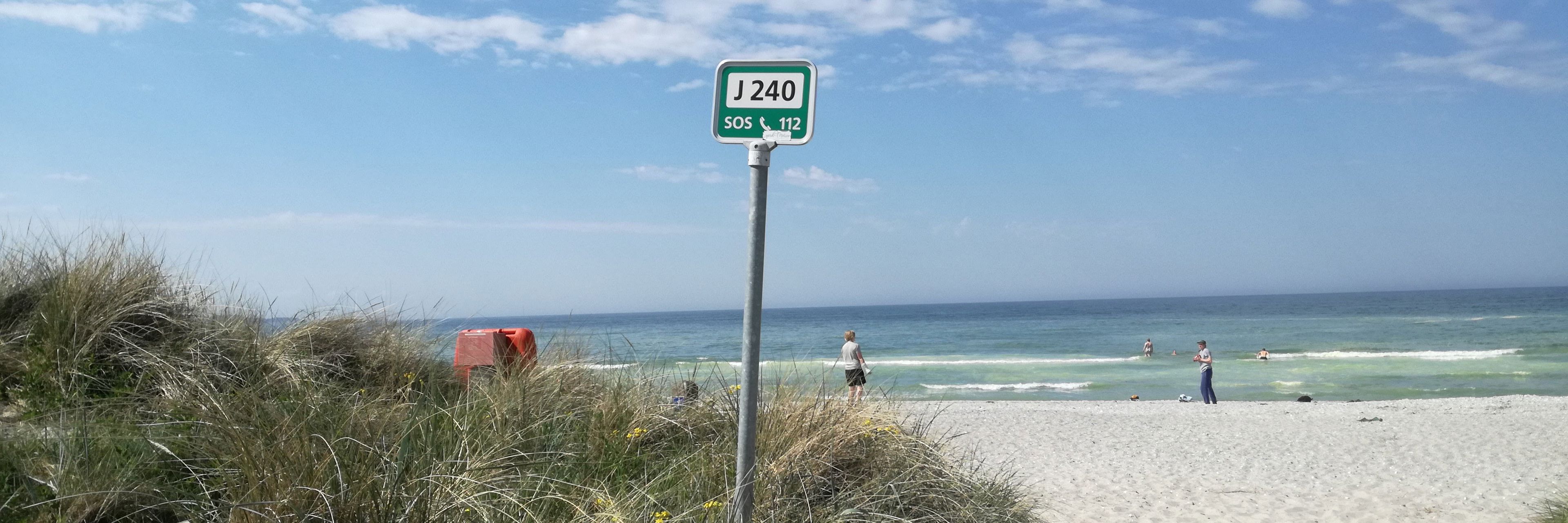 Skilt med redningsnummer på strand