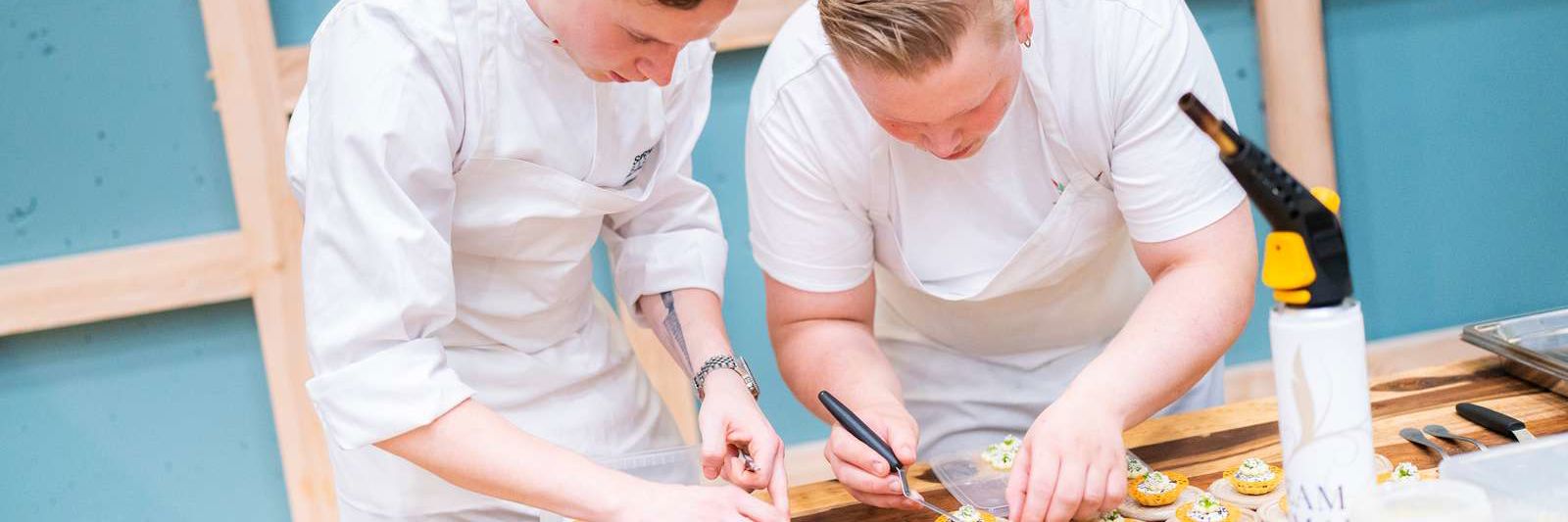 To kokke står bøjet over anretterbordet