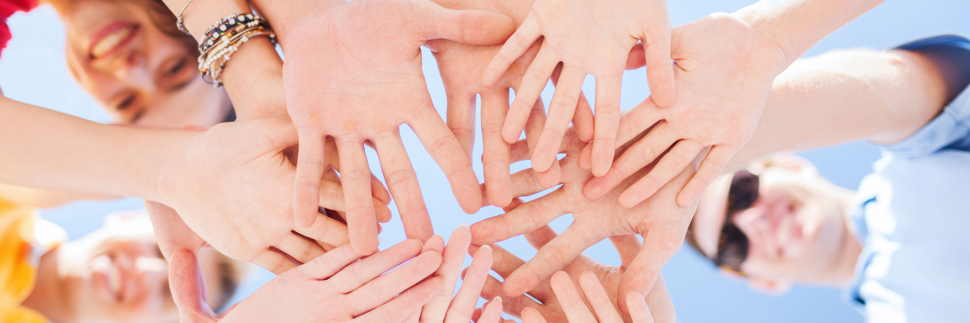 mennesker som står i en cirkel og rækker hænderne ud i midten. Man ser det nedfra.