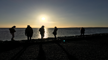 Unge mennesker ved havet ved solopgang