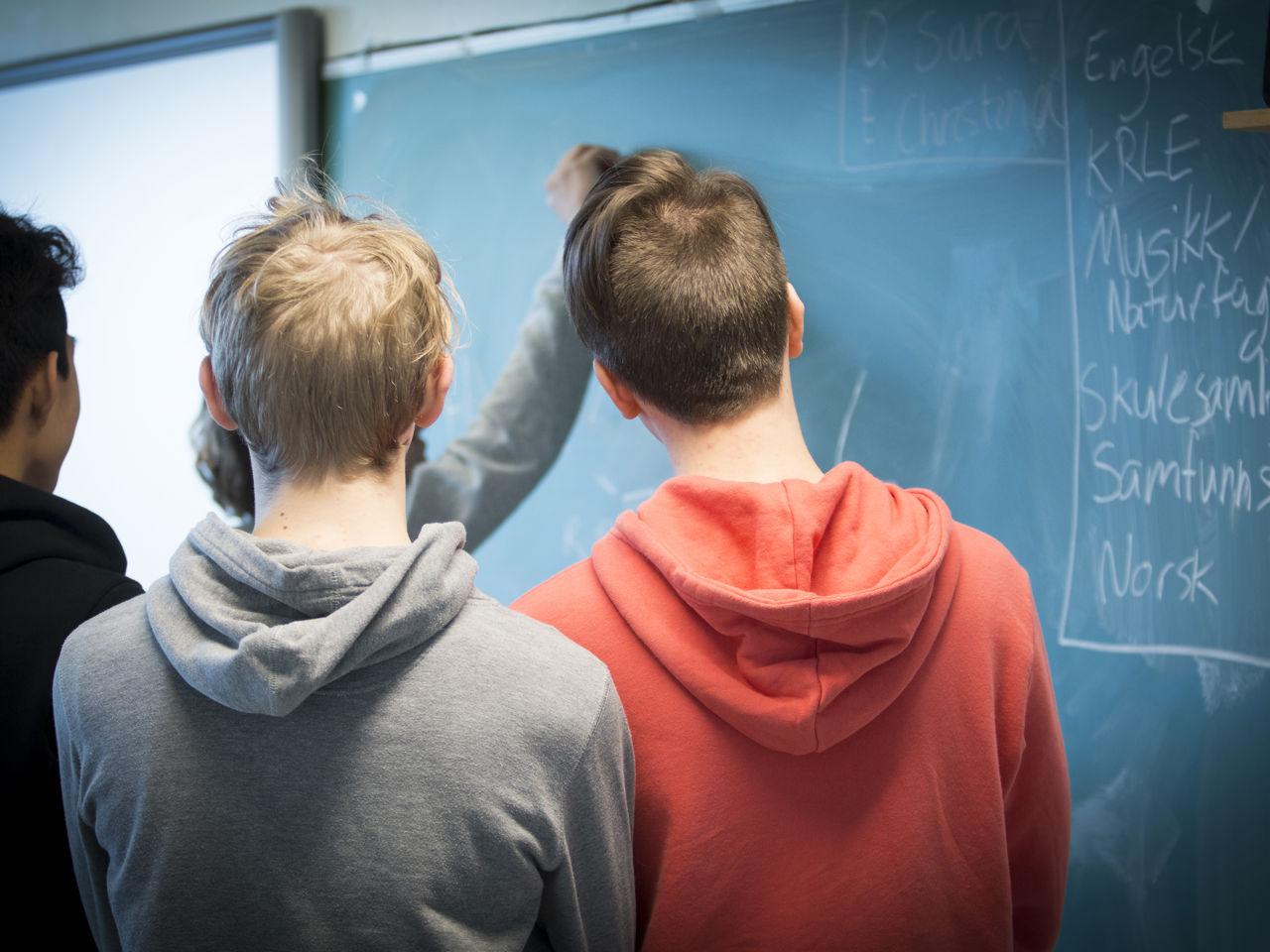 Teenagedrenge med ryggen til kigger på en skoletavle