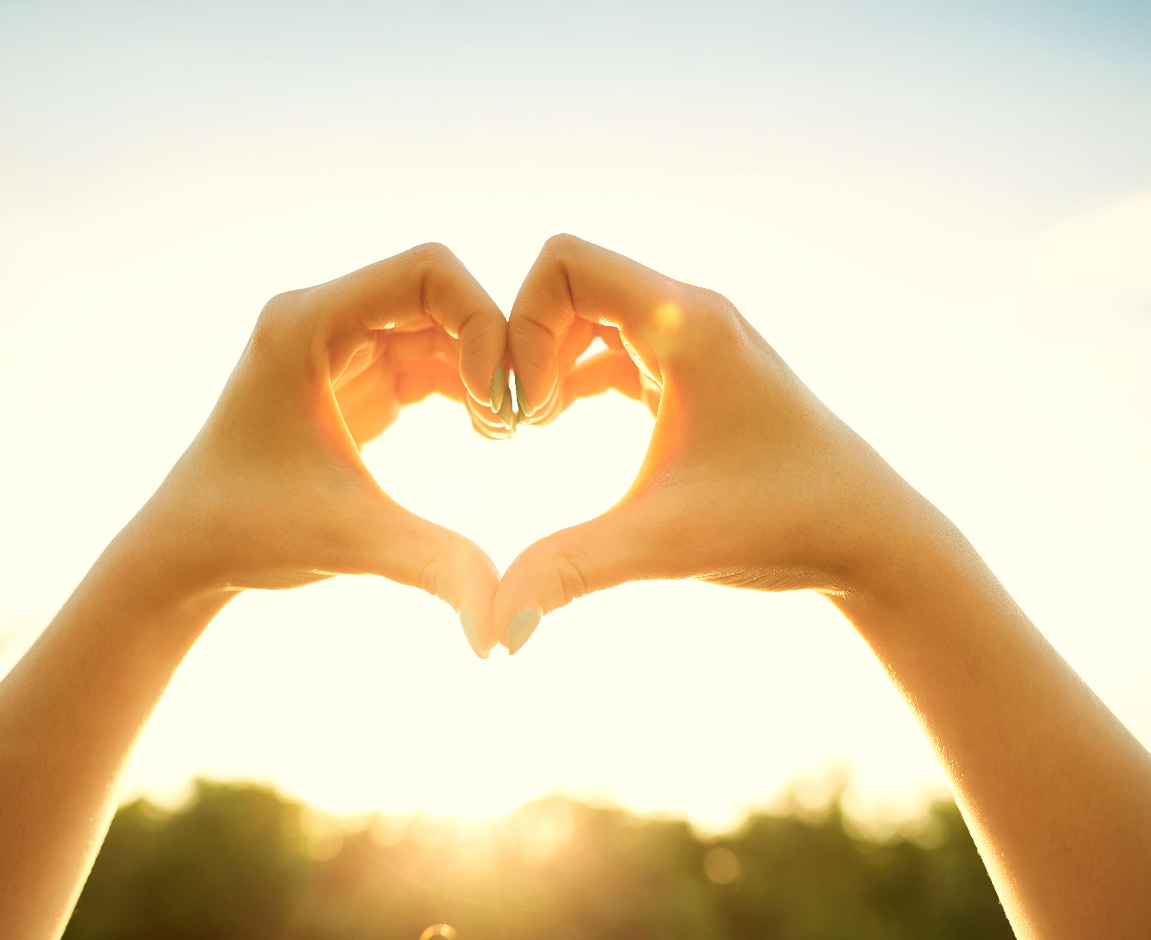 Hænder danner hjerte i modlys fra solen
