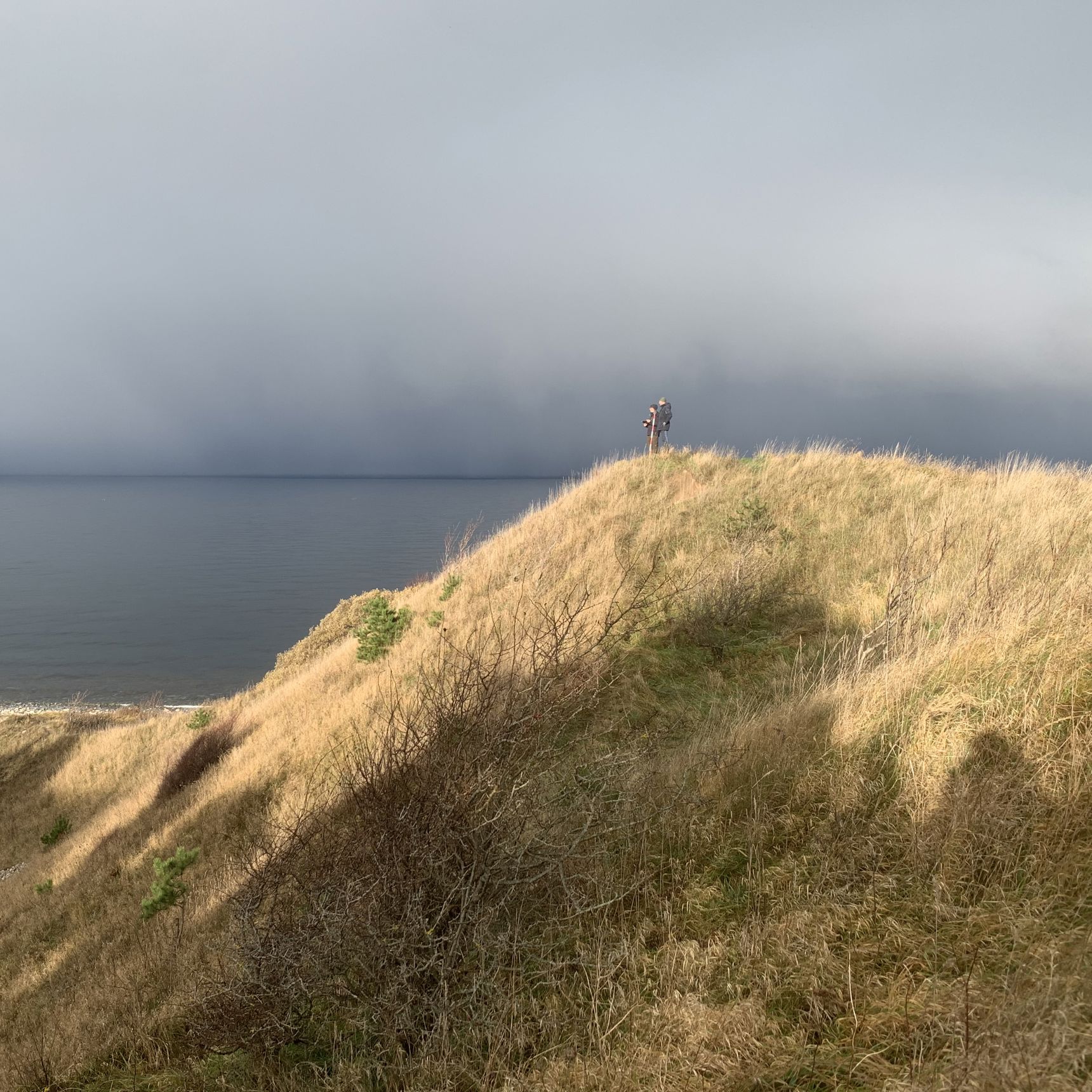 To mennesker på tommen af Klintebjerg på en solrig dag med havet baggrunden