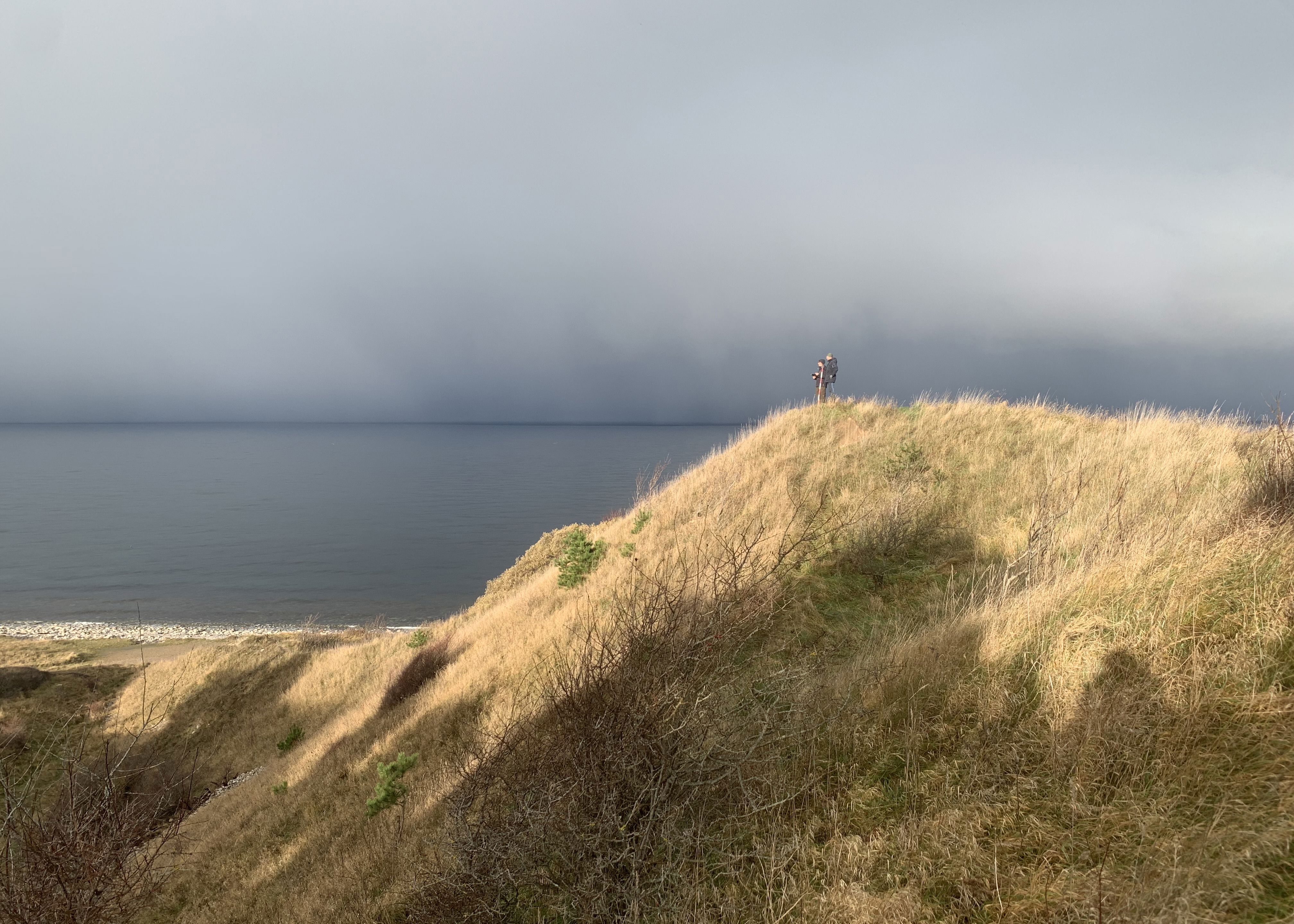 To mennesker på tommen af Klintebjerg på en solrig dag med havet baggrunden