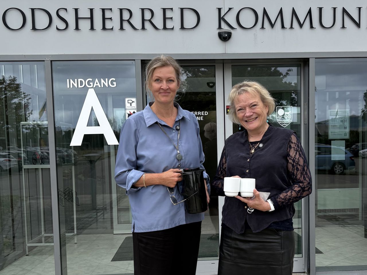 Kommunaldirektør Mette Touborg og borgmester Hanne Pigonska foran rådhuset med en termokande og to kopper