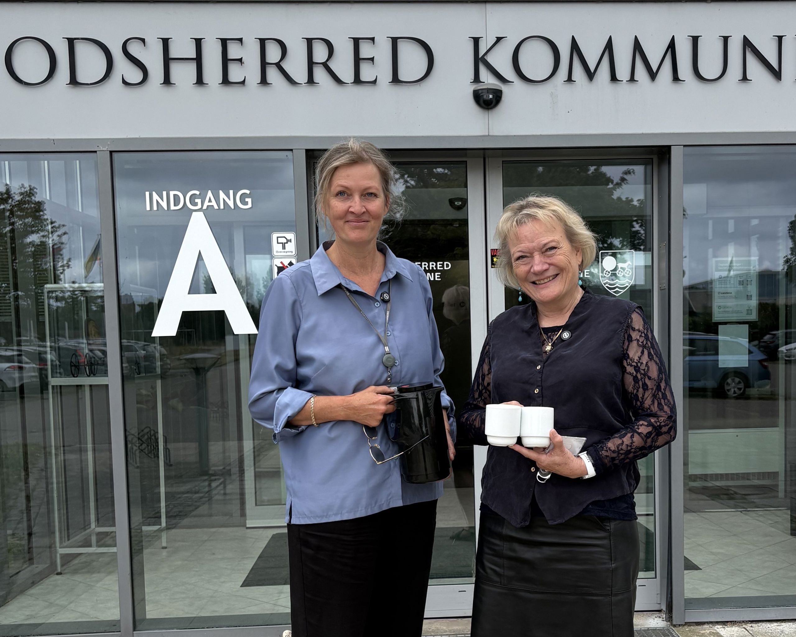 Kommunaldirektør Mette Touborg og borgmester Hanne Pigonska foran rådhuset med en termokande og to kopper