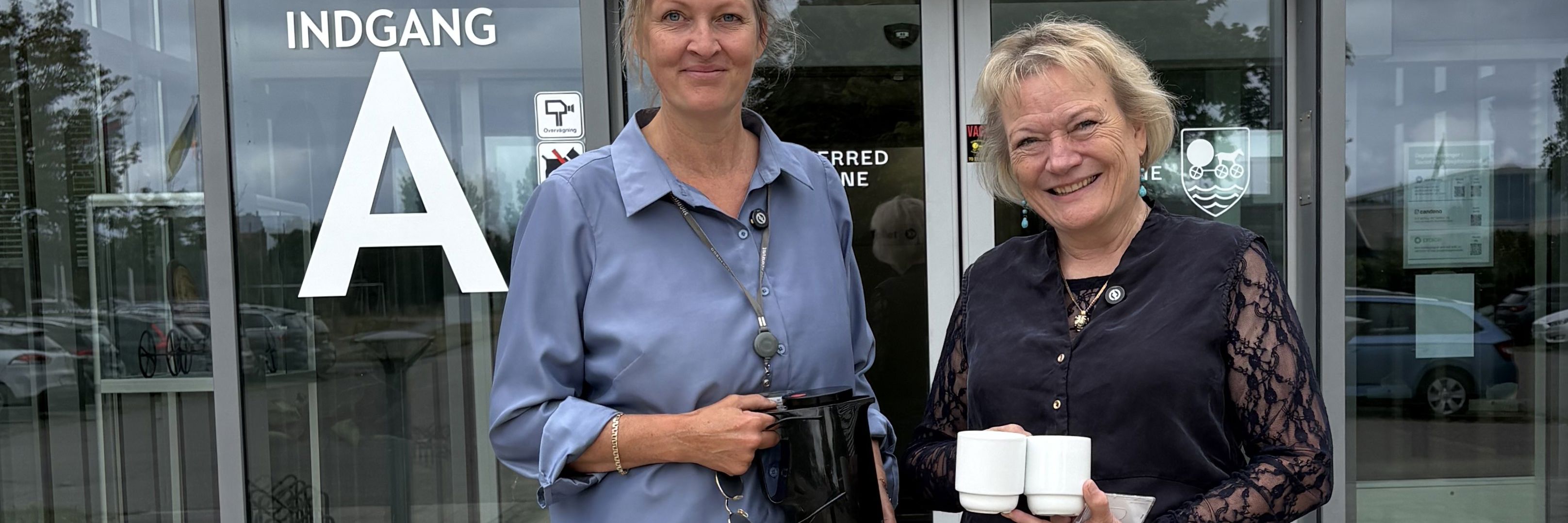 Kommunaldirektør Mette Touborg og borgmester Hanne Pigonska foran rådhuset med en termokande og to kopper