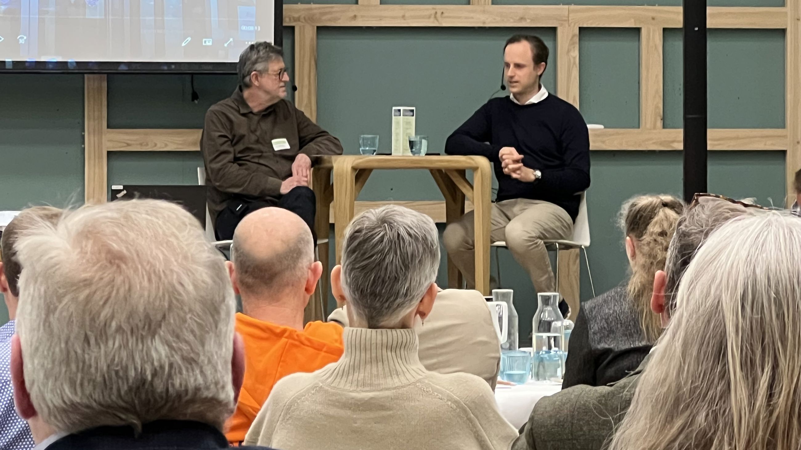 To mænd sidder ved et bord på en scene og taler