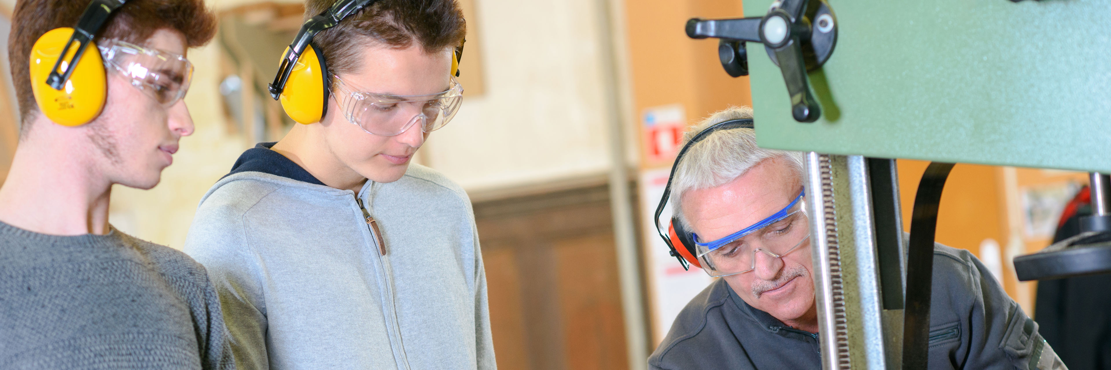 To unge mænd undervises i brug af maskine på værksted